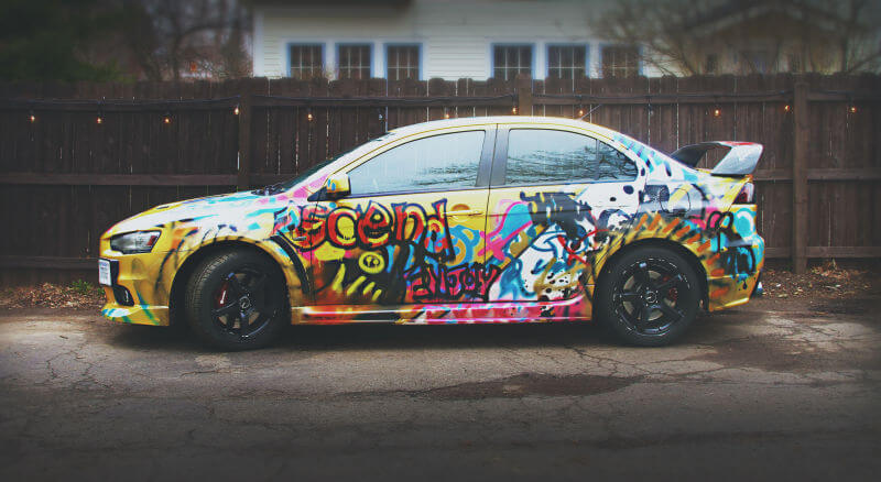 A car covered in graffiti parked in front of a fence
