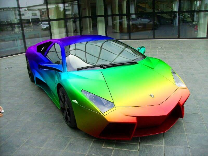 A rainbow colored sports car parked in front of a building
