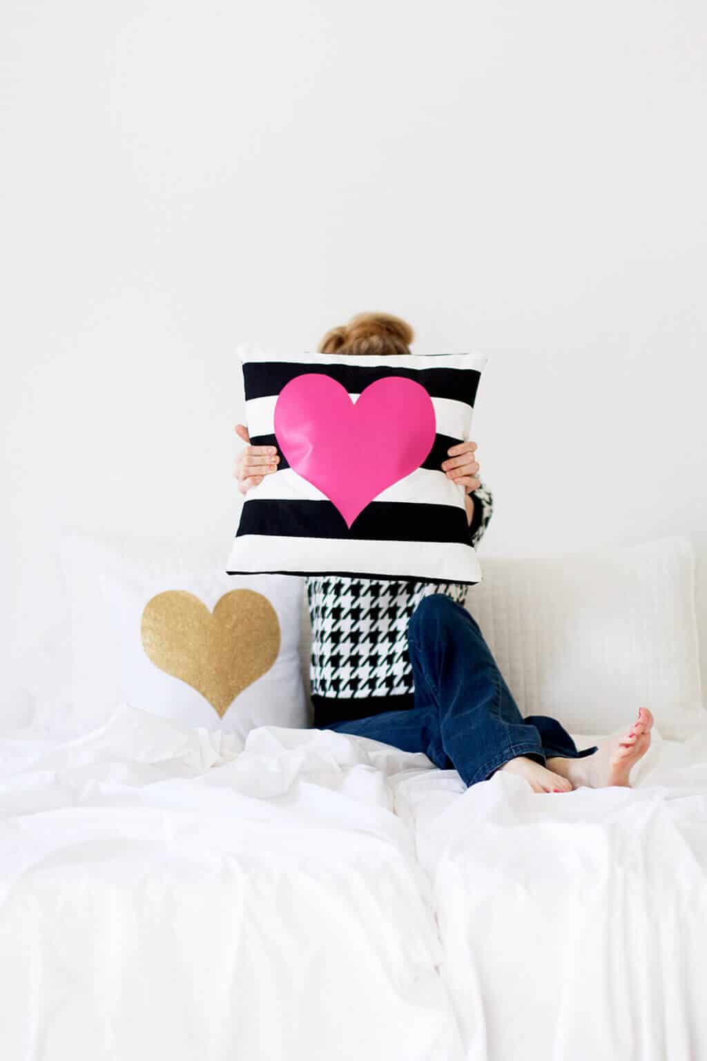 A person sitting on a bed holding a pillow with a heart on it
