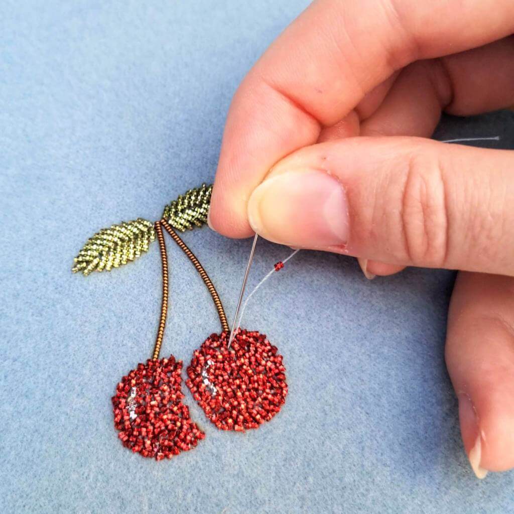 A pair of red beaded cherries being worked on
