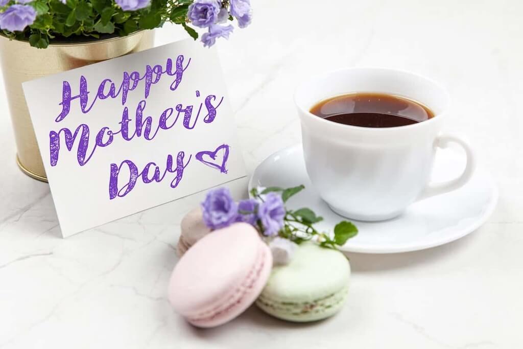 A happy mother's day card next to a cup of coffee and macaro
