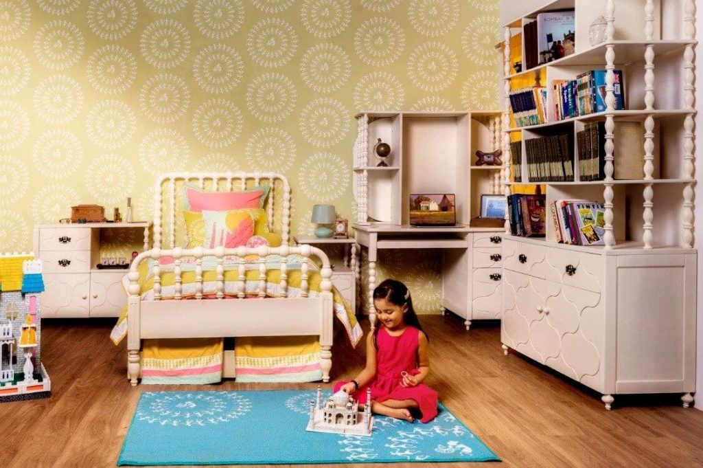 A little girl sitting on a blue rug in a bedroom
