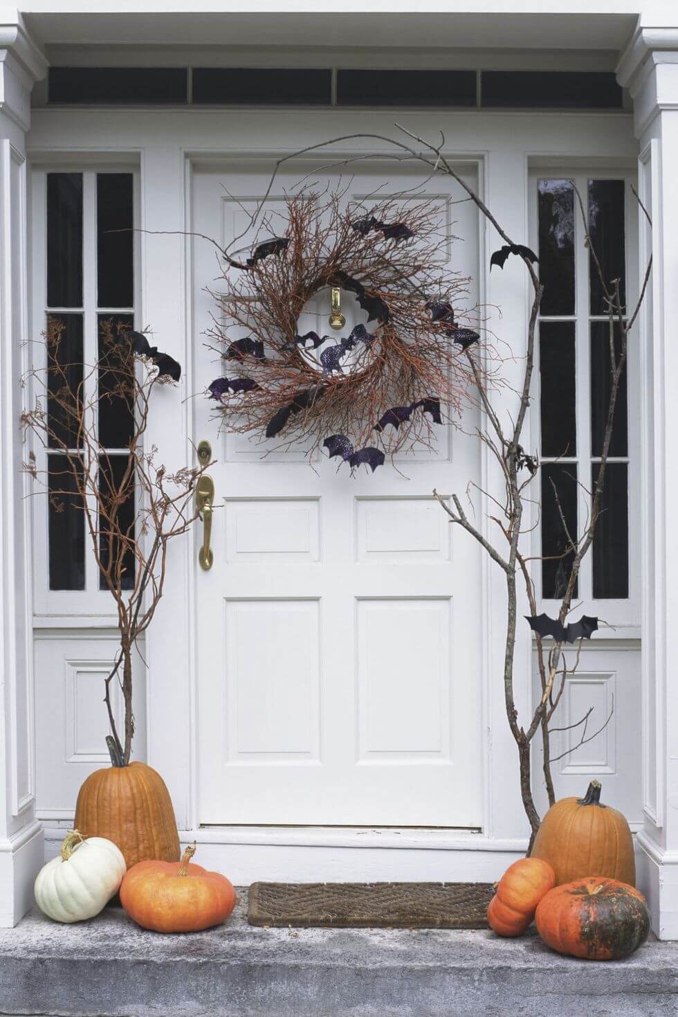 A front door decorated with pumpkins and branches
