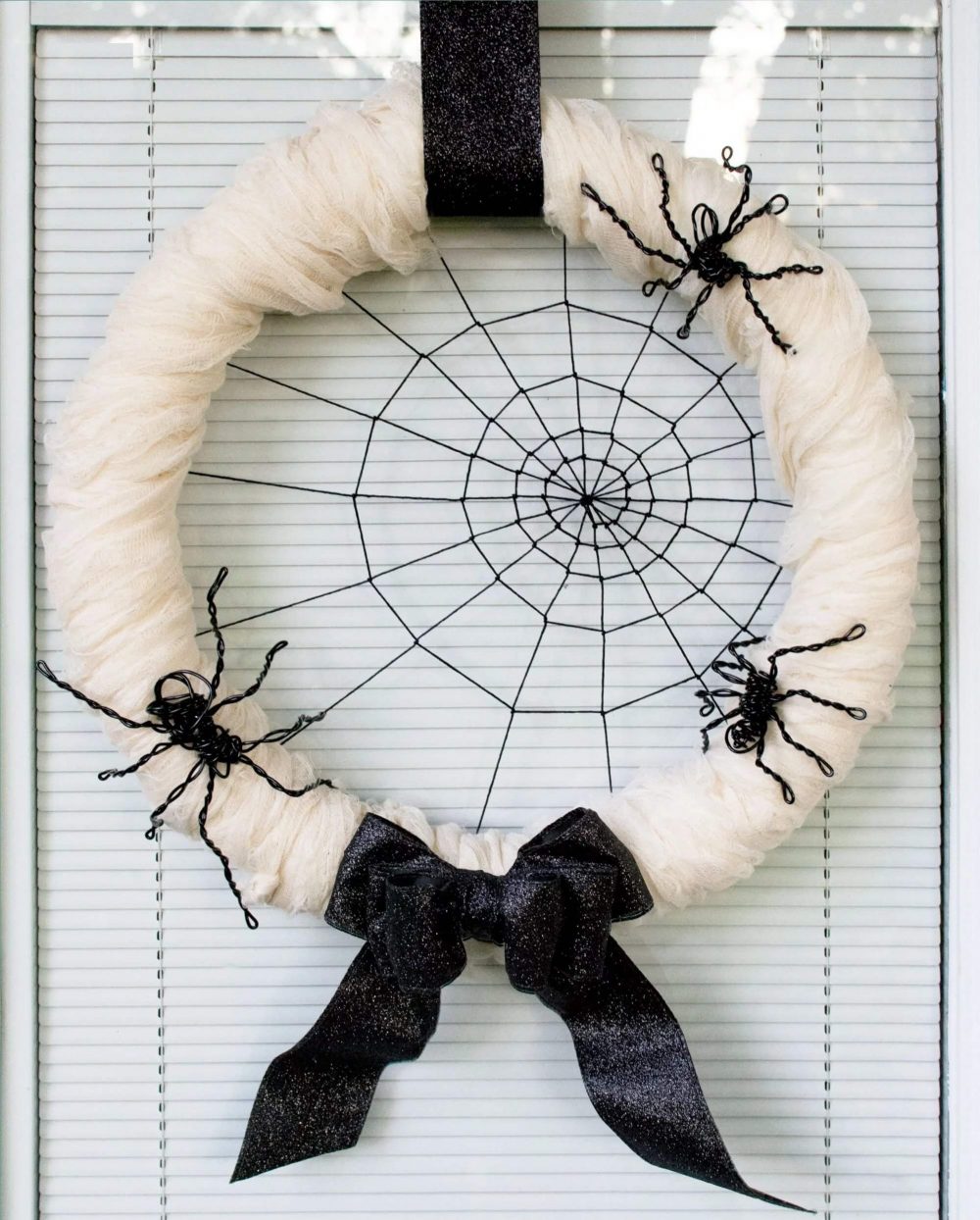 A white wreath with a black bow hanging on a door
