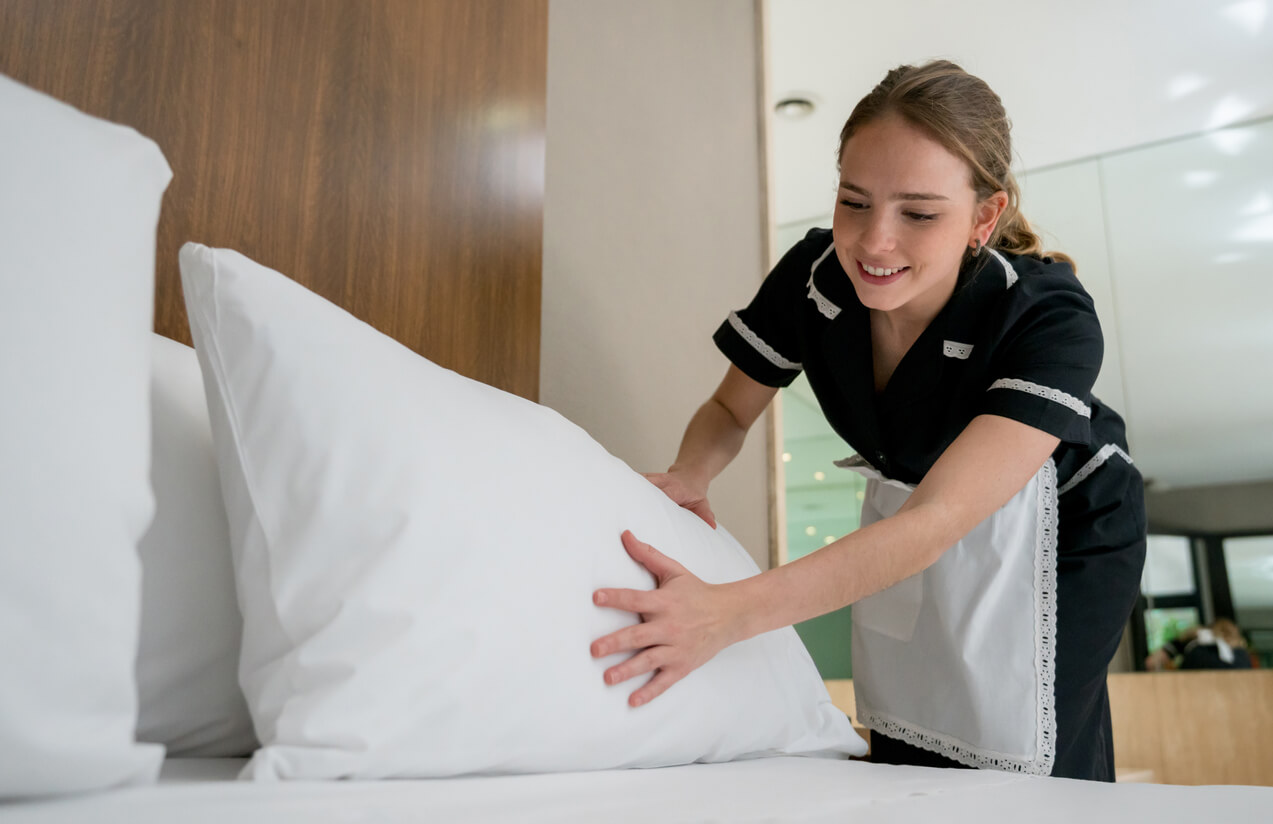 A woman placing a pillow on top of a bed
