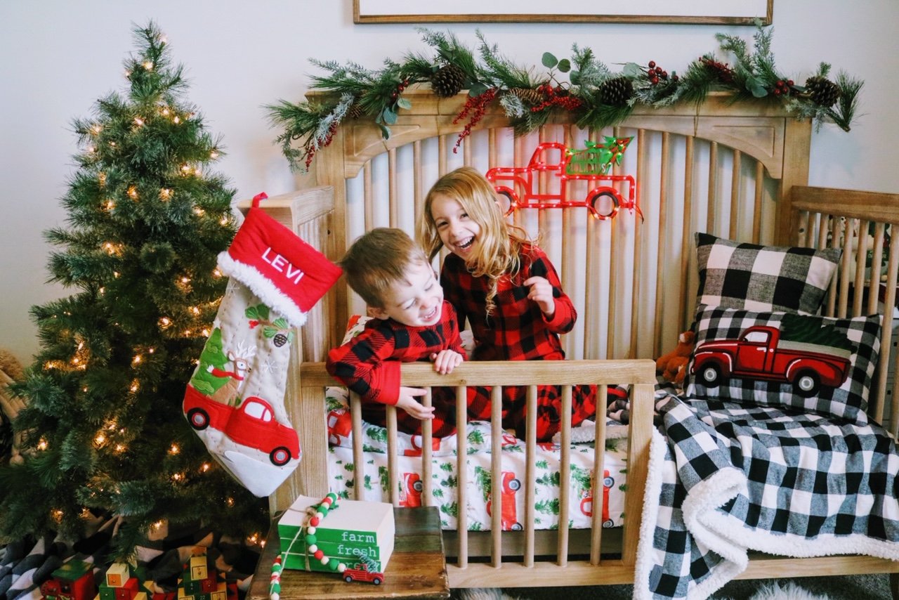 A couple of kids that are in a crib with a small christmas tree
