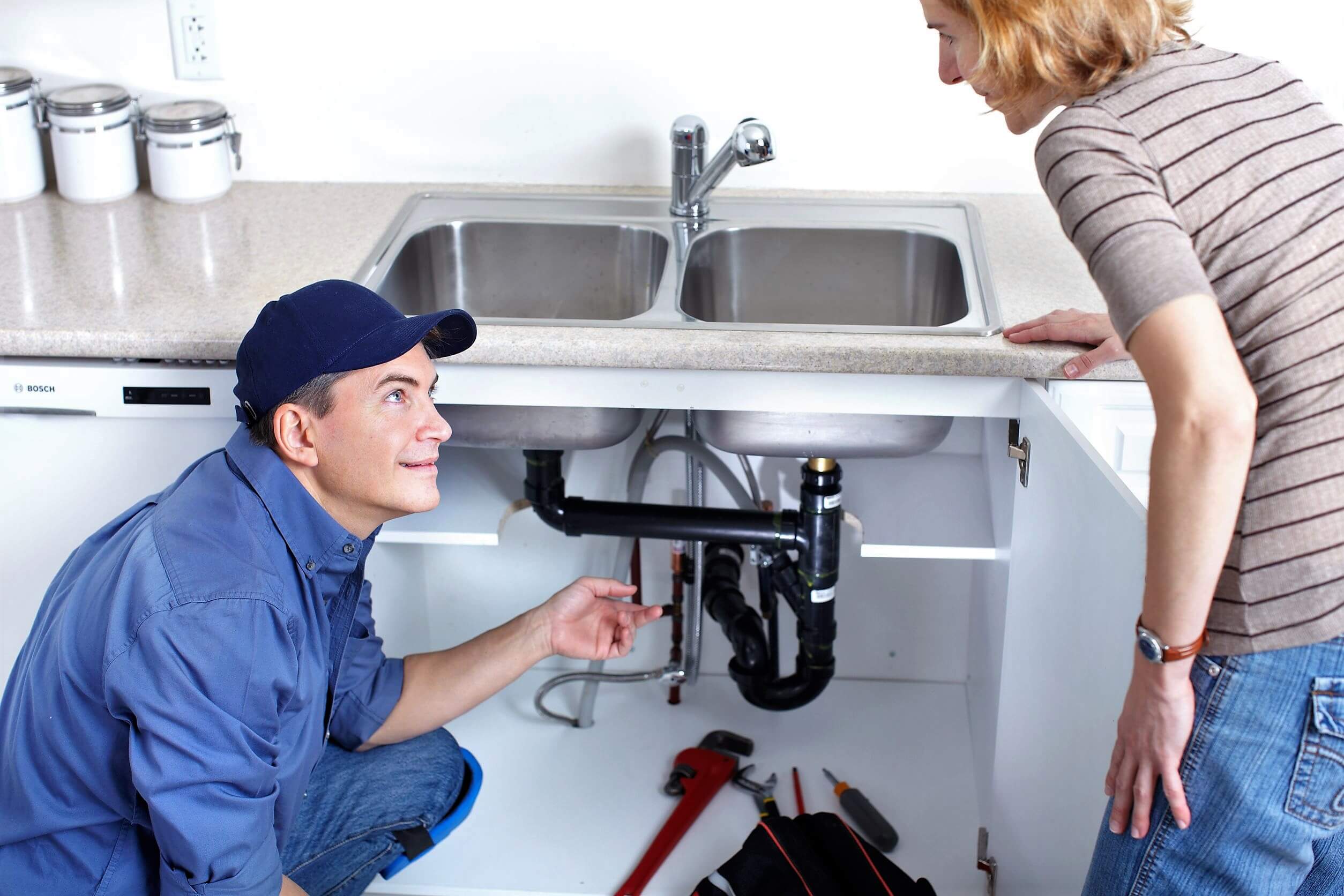 A man and a woman fixing a sink in a kitchen
