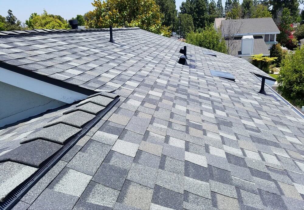 The Asphalt Shingles roof of a house with a black gutter
