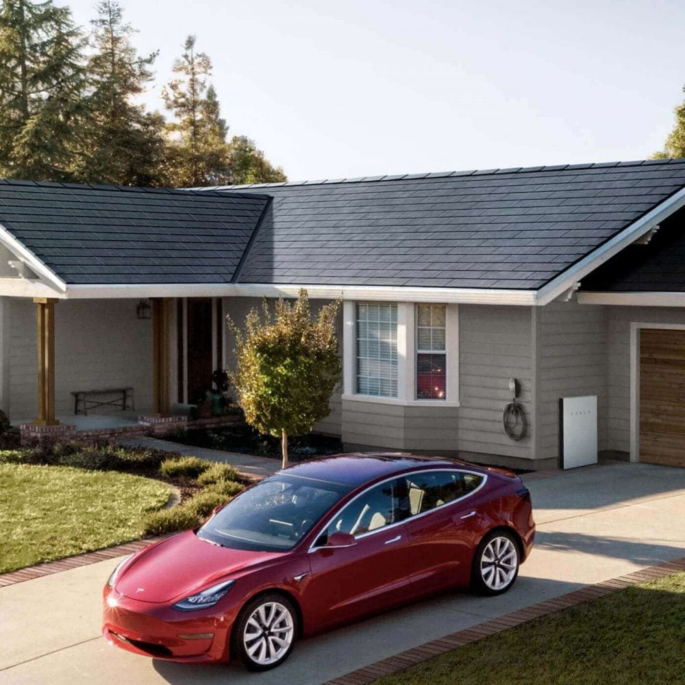 A red tesla parked in front of a house with Solar Glass Roof 
