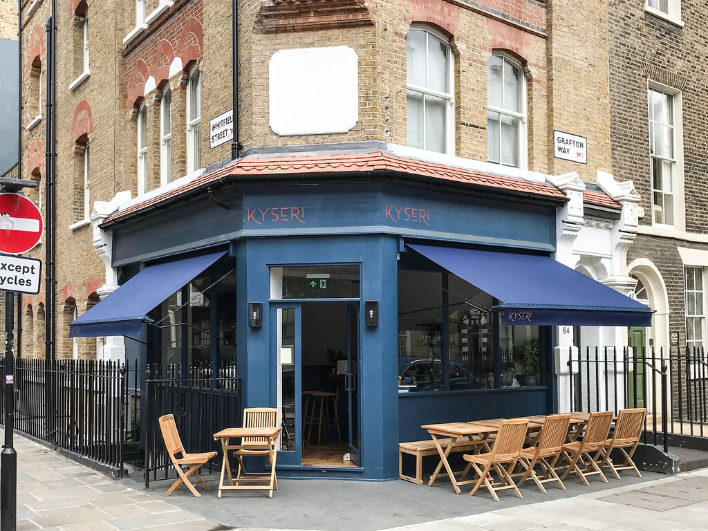 A blue shop with tables and chairs outside of it

