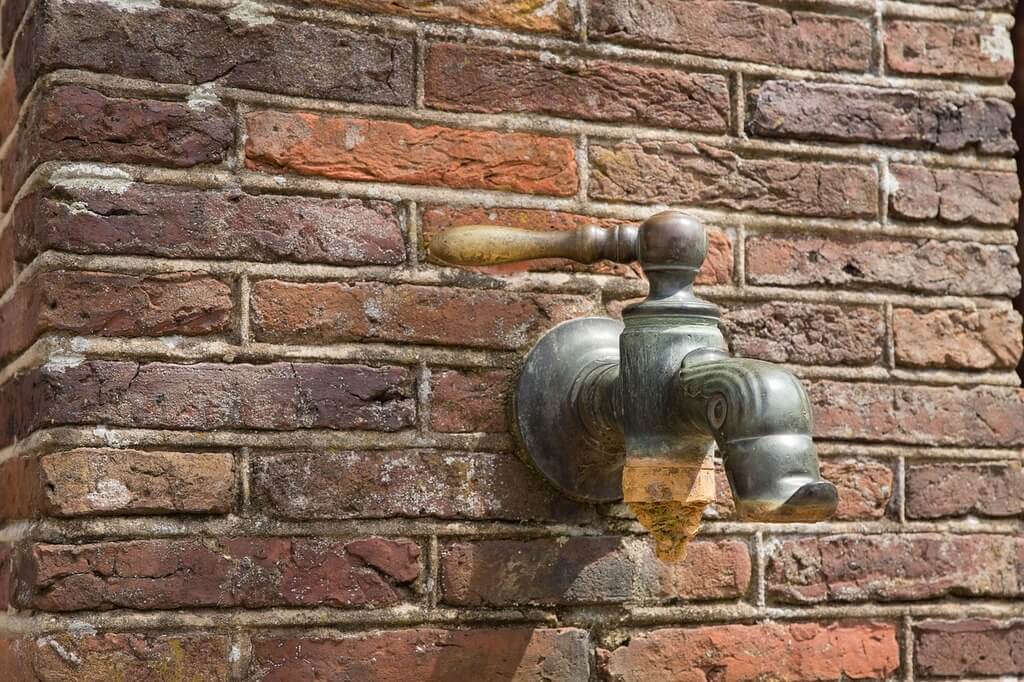 A water faucet attached to a brick wall

