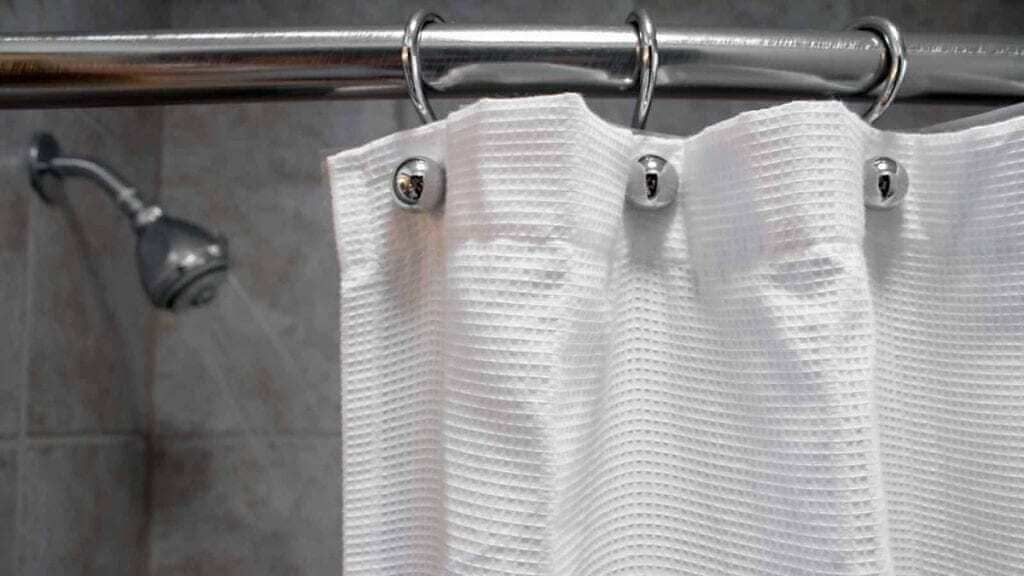 A white shower curtain hanging from a metal rod
