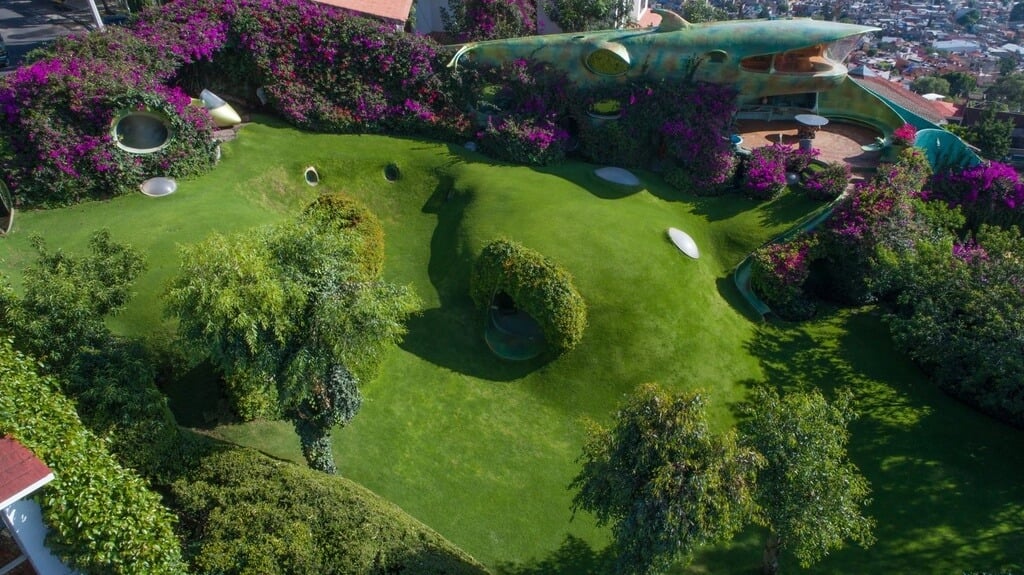 An aerial view of a organic house in the middle of a lush green area
