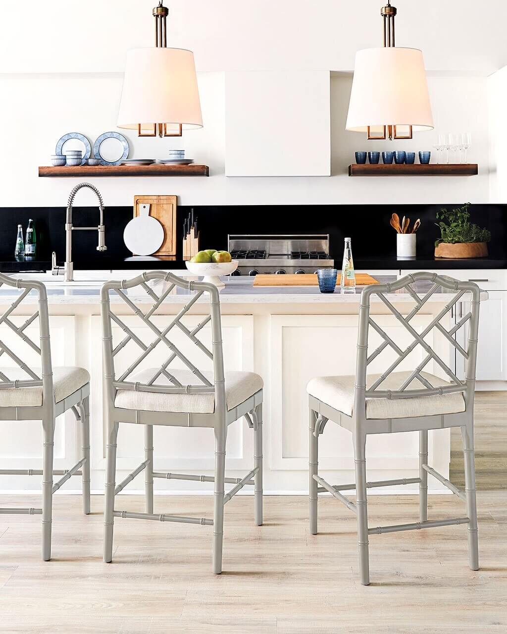 A white kitchen with a center island and three chairs
