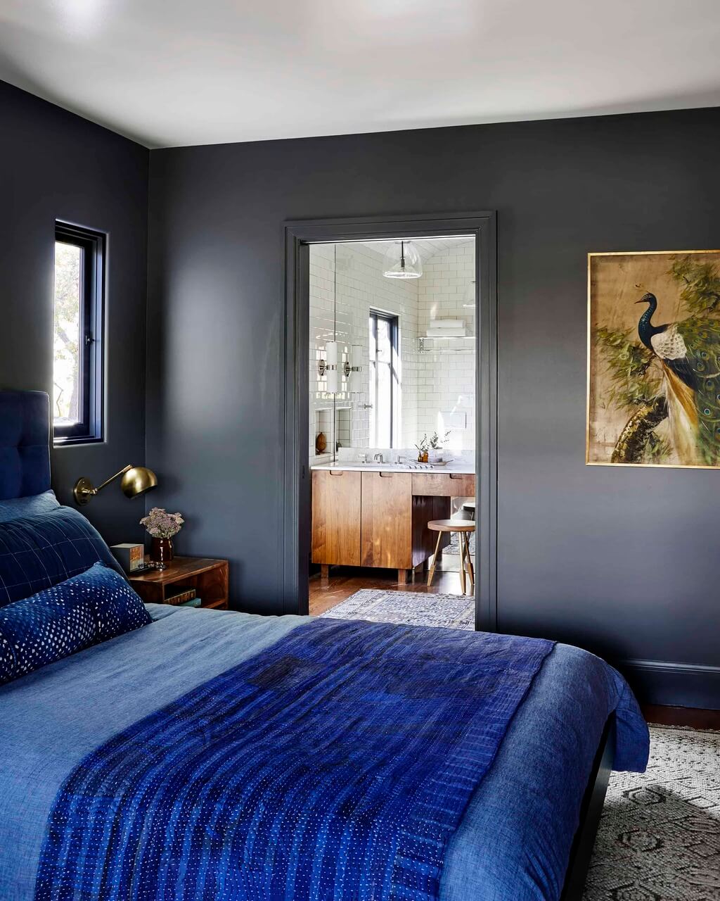 A bedroom with a blue bed and a painting on the wall

