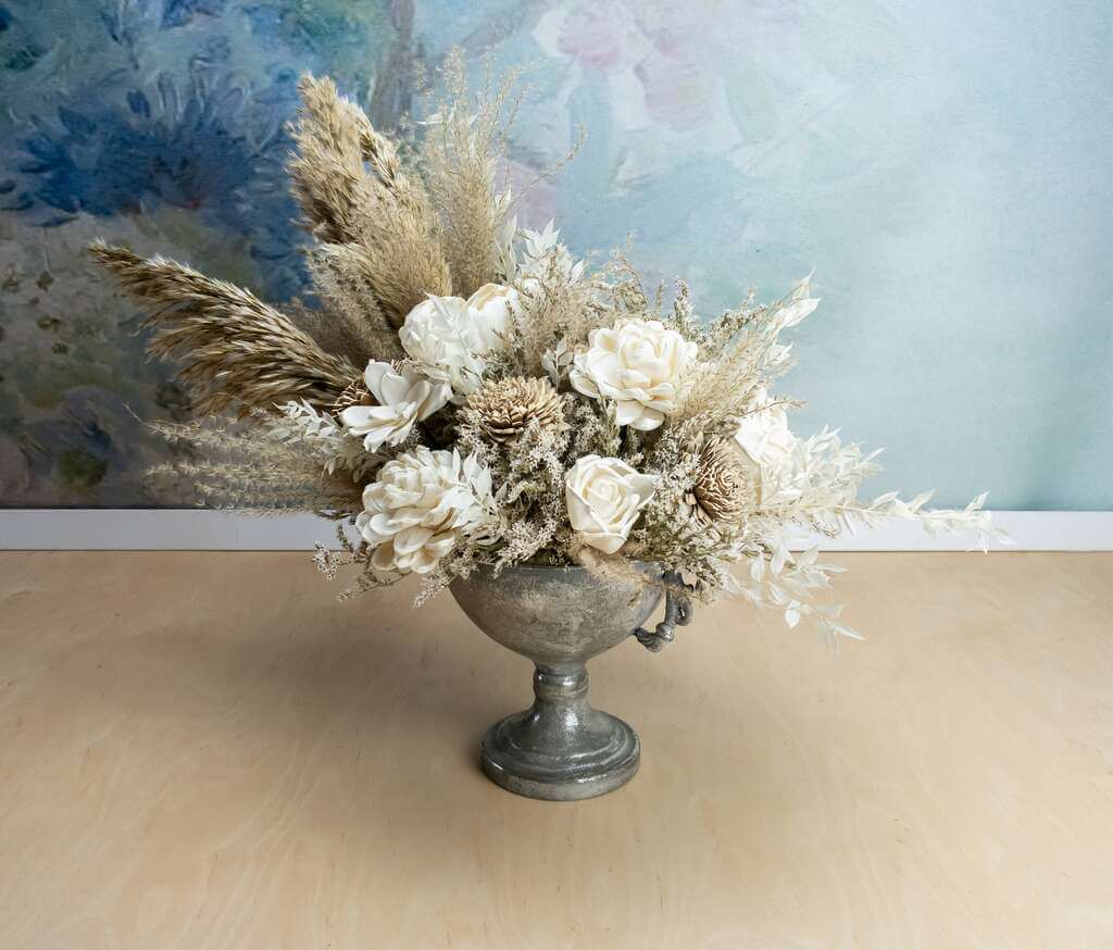 A silver vase filled with white flowers on top of a wooden table
