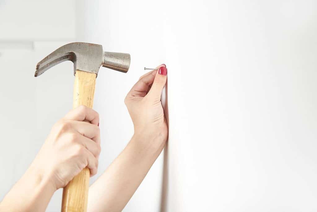 A woman holding a hammer on a white wall.
