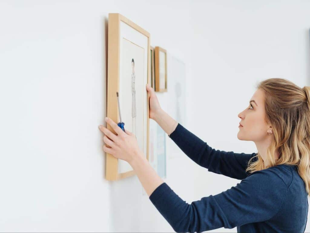 A woman is hanging a picture on the wall.