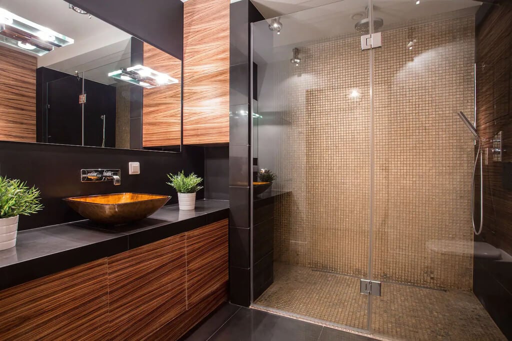 A bathroom with a glass shower door and a wooden sink
