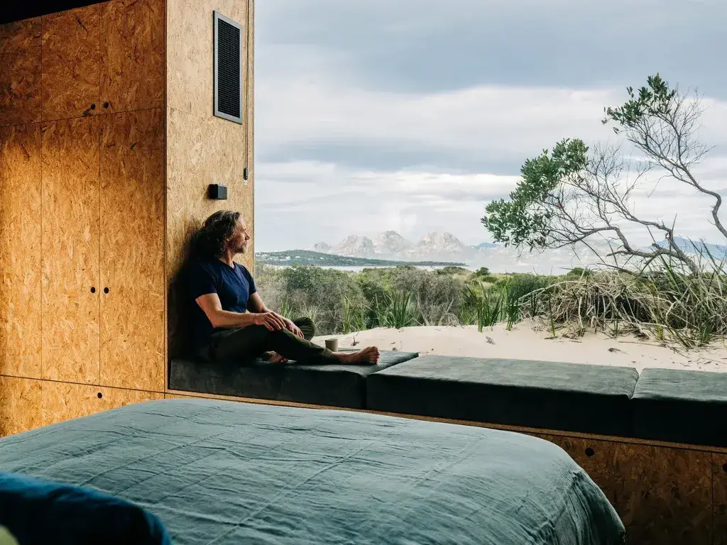 A man sitting on a bed looking out a window
