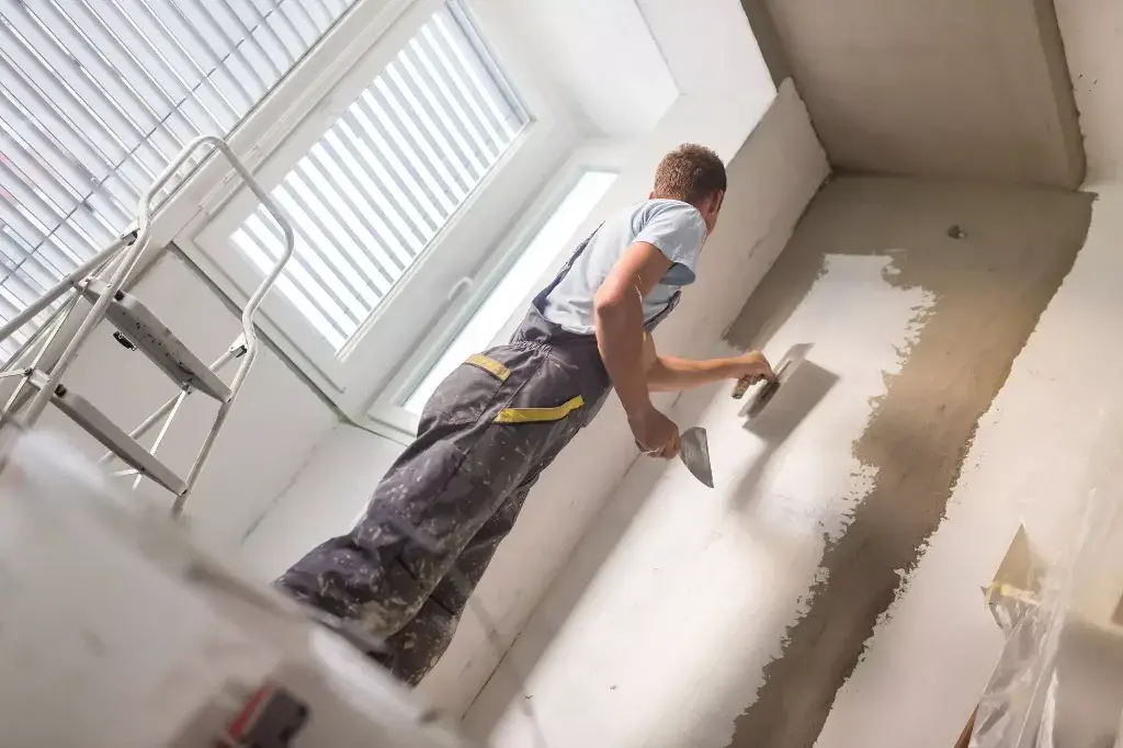 Stucco Repair : A man in overalls painting a wall with a paint roller
