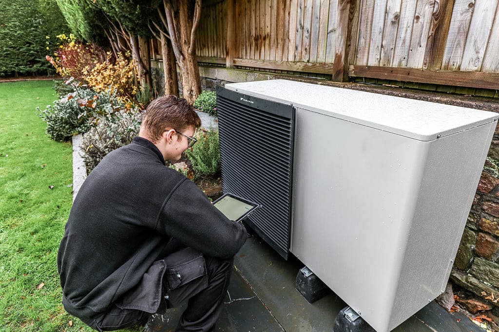 A man kneeling down next to an air conditioner
