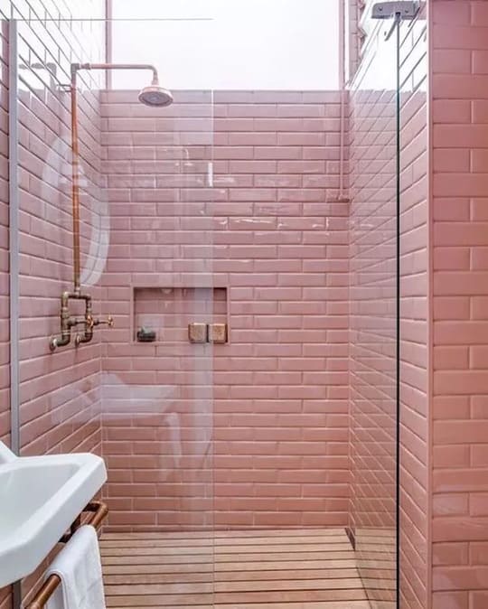 A bathroom with a pink brick wall and wooden floor
