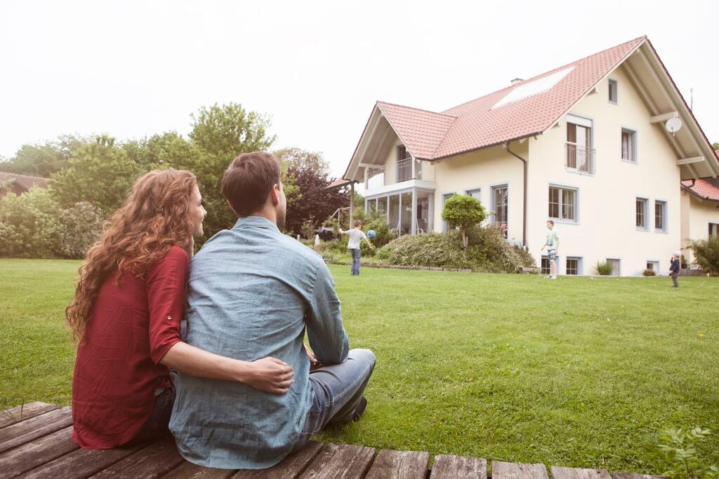 A couple sitting on a bench in front of a house.