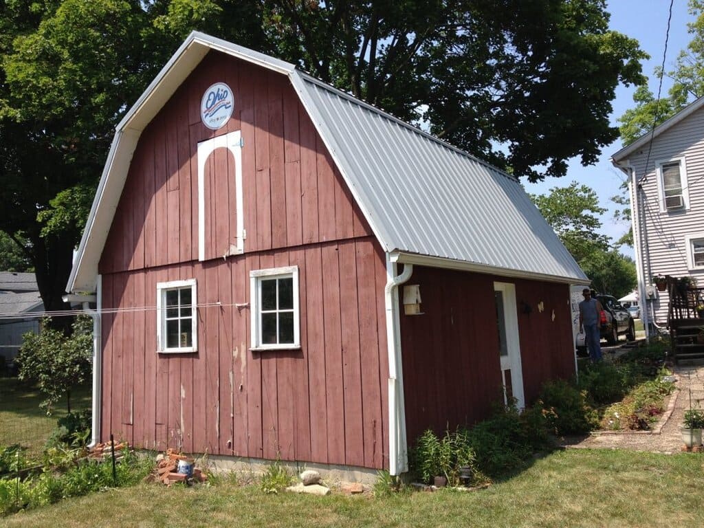 A red barn with Gambrel Roof Designs and  a clock on the side of it
