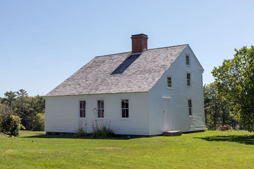 A white house with Saltbox Roofs sitting on top of a lush green field
